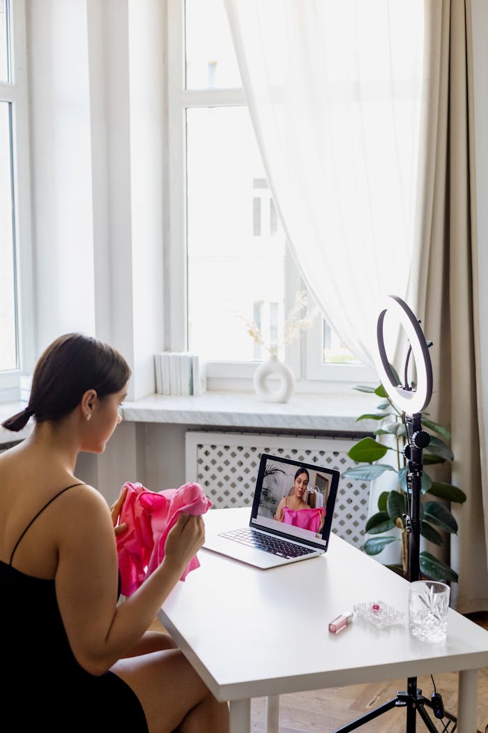 who-we-are A young woman creates fashion vlog content at home with a laptop and ring light.
